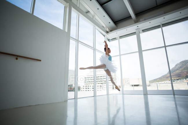 Прыжки балерины во время репетиции балета в студии с окнами — стоковое фото