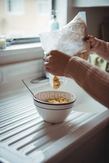 Mulher derramando cereais em uma tigela na cozinha — Fotografia de Stock