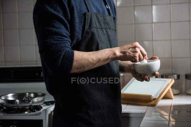 Meados de seção do homem usando pilão e argamassa na cozinha em casa — Fotografia de Stock