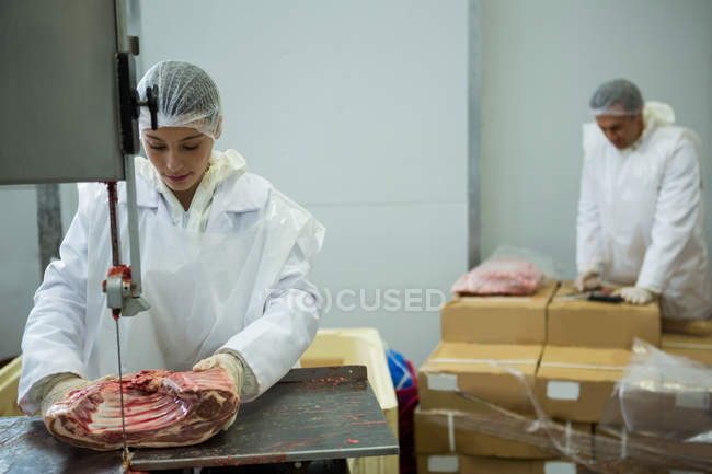 Female butcher cutting meat with meat cutting machine at meat factory — Stock Photo