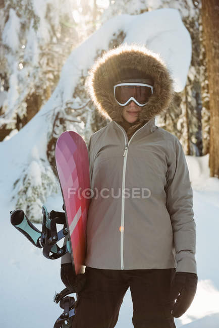 Woman standing and holding a snowboard on snow covered mountain — Stock Photo