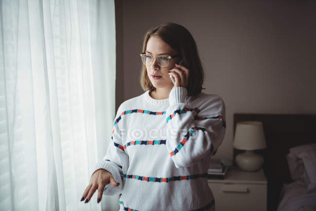 Mujer de pie en el dormitorio y hablando por teléfono móvil en casa - foto de stock