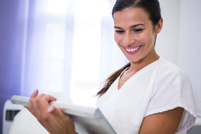 Dentiste souriant utilisant une tablette numérique en clinique — Photo de stock