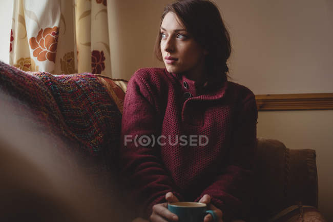 Thoughtful woman sitting and holding a coffee cup at home — Stock Photo