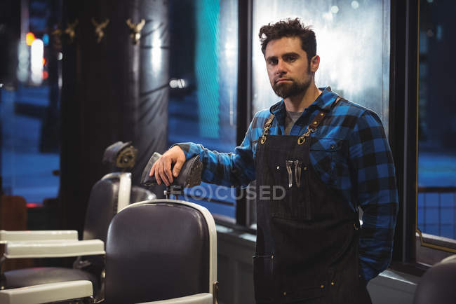 Portrait of male barber standing near chair in barber shop — Stock Photo