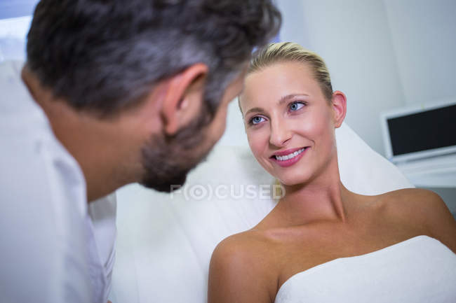 Paciente femenina sonriendo mientras mira al médico en la clínica - foto de stock
