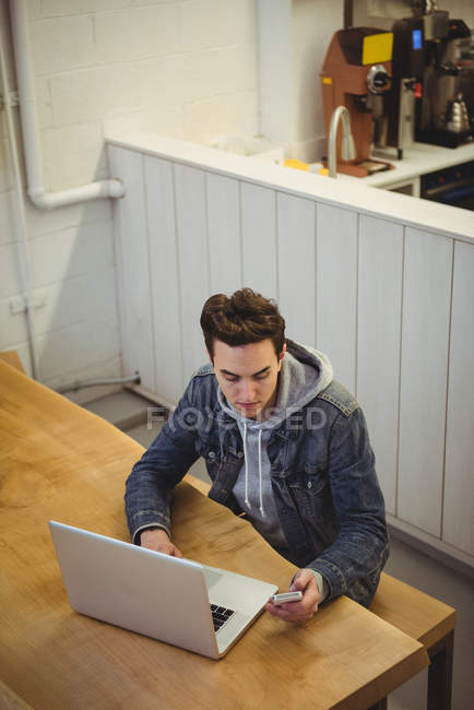 Uomo che utilizza il telefono cellulare e laptop in caffetteria — Foto stock