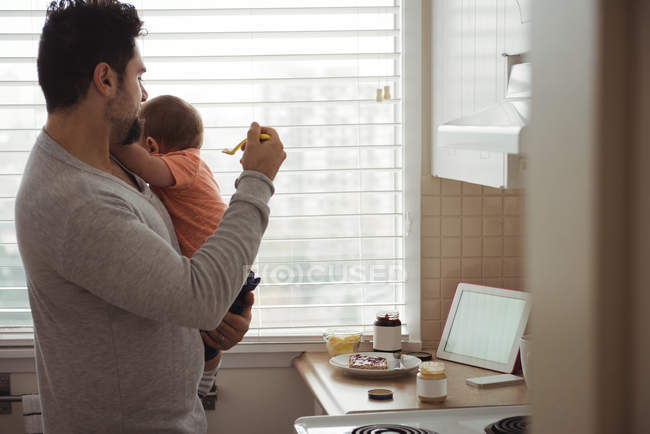 Father feeding baby boy with spoon in kitchen at home — Stock Photo