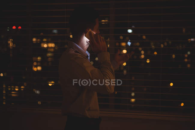 Uomo che guarda attraverso la finestra mentre parla sul cellulare di notte — Foto stock