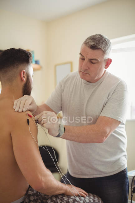 Fisioterapista che esegue aghi elettro-asciutti sulla spalla del paziente maschio in clinica — Foto stock