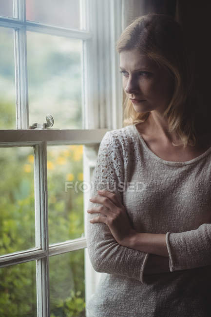 Задумчивая женщина, стоящая у окна дома — стоковое фото
