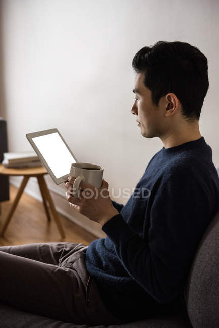 Homem usando tablet digital enquanto toma café em casa — Fotografia de Stock