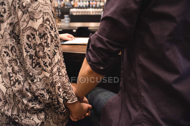 Sezione centrale della coppia seduta al bancone del bar e che si tiene per mano — Foto stock