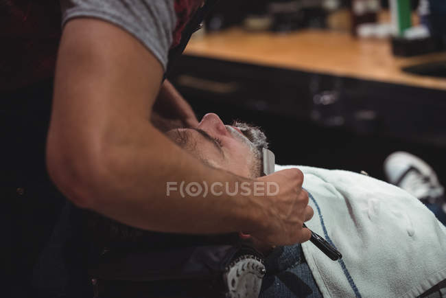 Мужчина сбривает бороду бритвой в парикмахерской — стоковое фото