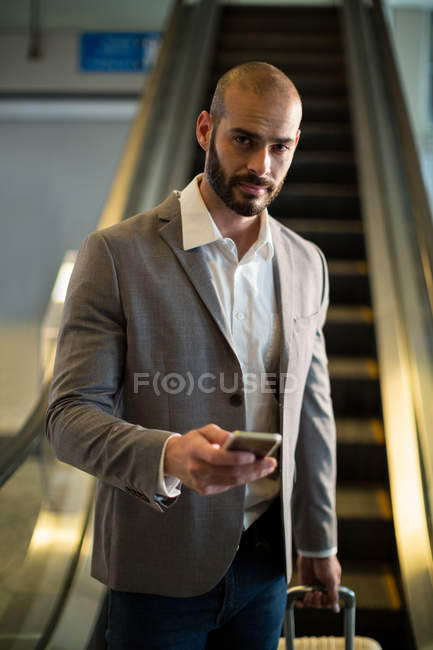 Retrato de homem de negócios com bagagem usando telefone celular no aeroporto — Fotografia de Stock