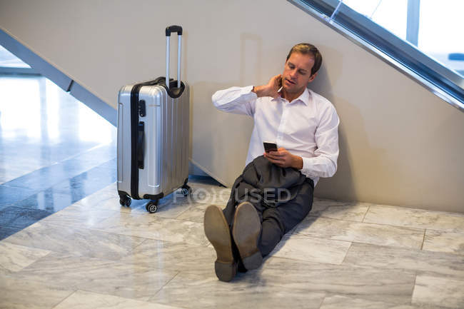 Businessman sitting on floor and using mobile phone in waiting area at airport terminal — Stock Photo