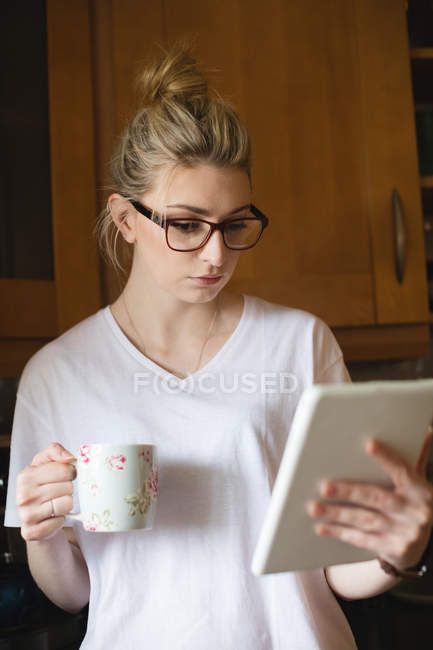Жінка використовує цифровий планшет, маючи каву на кухні вдома — стокове фото