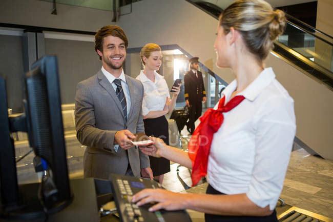 Бизнесмен, выдающий посадочный талон сотруднице женского пола на стойке регистрации в терминале аэропорта — стоковое фото