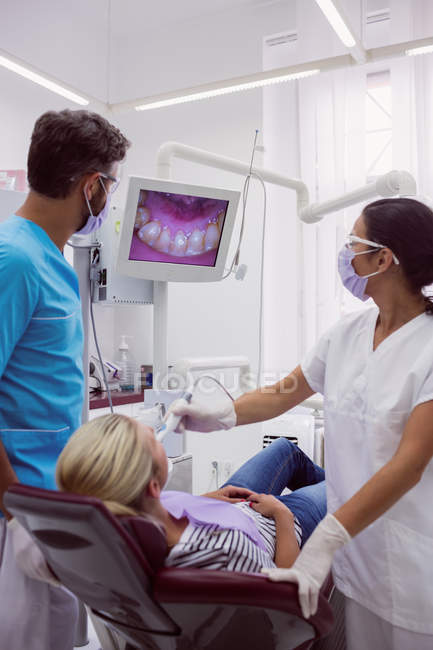 Odontólogos masculinos y femeninos examinando paciente en clínica dental - foto de stock