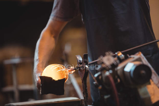 Mid section of glassblower forming and shaping a molten glass at glassblowing factory — Stock Photo