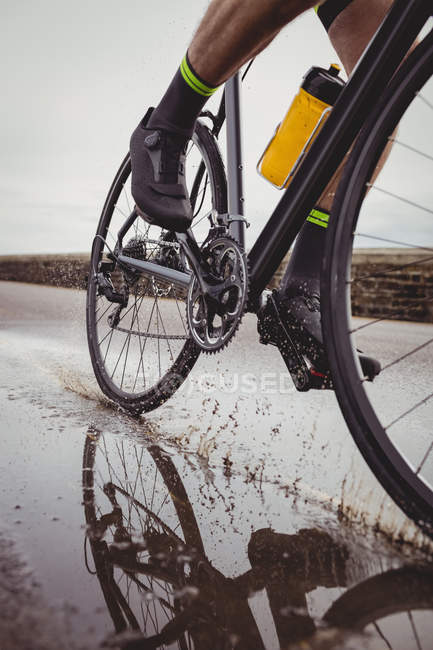 Bassa sezione di atleta in bicicletta su strada bagnata — Foto stock