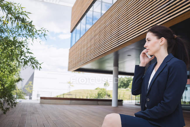 Businesswoman sitting outside office building and talking on mobile phone — Stock Photo