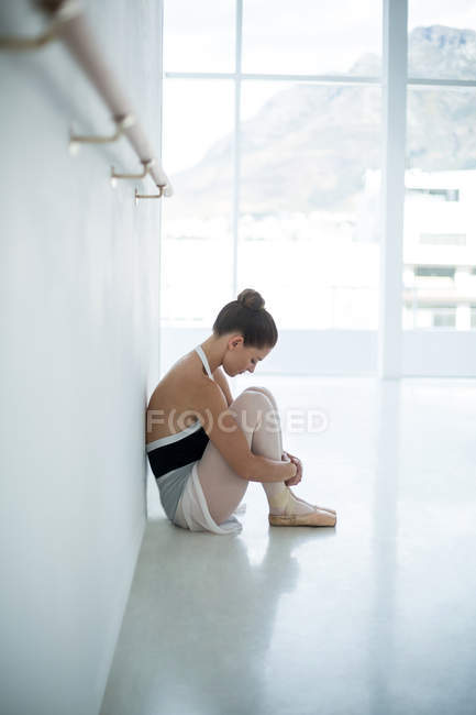 Печальная балерина сидит на полу в балетной студии — стоковое фото