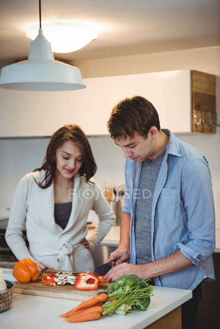 Pareja de cortar verduras juntos en la cocina en casa - foto de stock