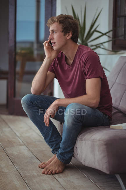 Чоловік сидить на дивані і говорить на мобільному телефоні у вітальні — стокове фото