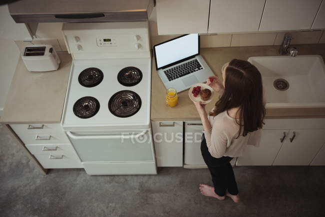 Frau schaut beim Frühstück in der heimischen Küche auf Laptop — Stockfoto