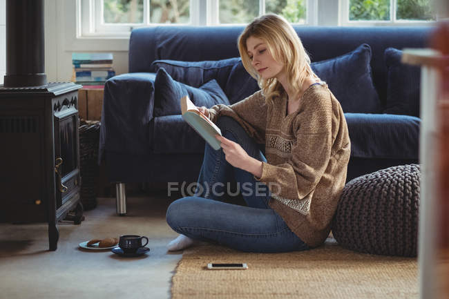 Красива жінка читає книгу, маючи чай у вітальні вдома — стокове фото