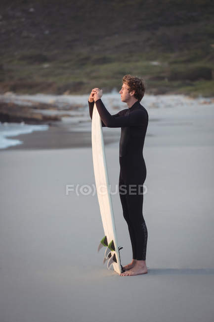 Side view of a man wearing wetsuit standing on beach with surfboard — Stock Photo