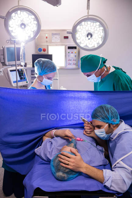 Equipo de médicos examinando a la mujer embarazada durante el parto en la sala de operaciones - foto de stock
