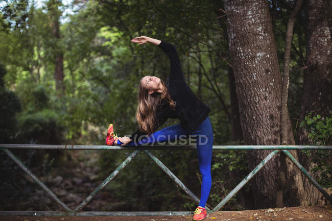 Жінка робить розтягування вправи на прохідному мосту в лісі — стокове фото