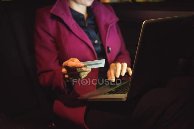 Businesswoman doing online shopping on laptop with credit card in car — Stock Photo