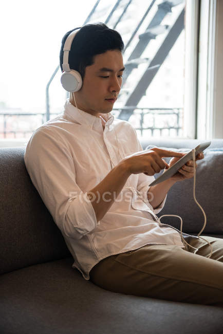 Hombre escuchando música en tableta digital en casa - foto de stock