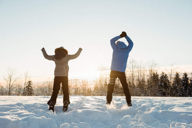 Visão traseira do casal pulando na paisagem nevada — Fotografia de Stock