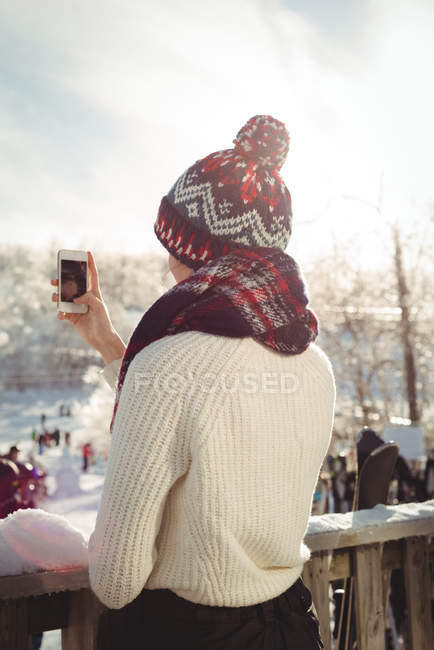 Vista posteriore della donna che scatta una fotografia utilizzando il telefono cellulare presso la stazione sciistica — Foto stock