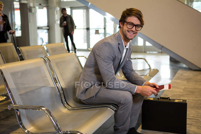 Uomo d'affari con passaporto, carta d'imbarco e valigetta seduto in sala d'attesa al terminal dell'aeroporto — Foto stock