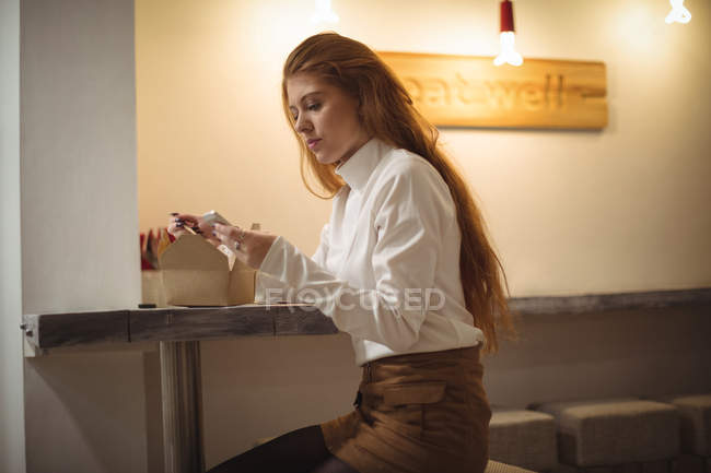 Beautiful woman using mobile phone while eating salad — Stock Photo