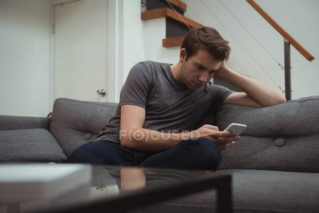 Homem usando telefone celular no sofá em casa — Fotografia de Stock