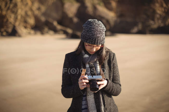 Femme regardant des photos sur l'appareil photo numérique à la plage pendant la journée — Photo de stock