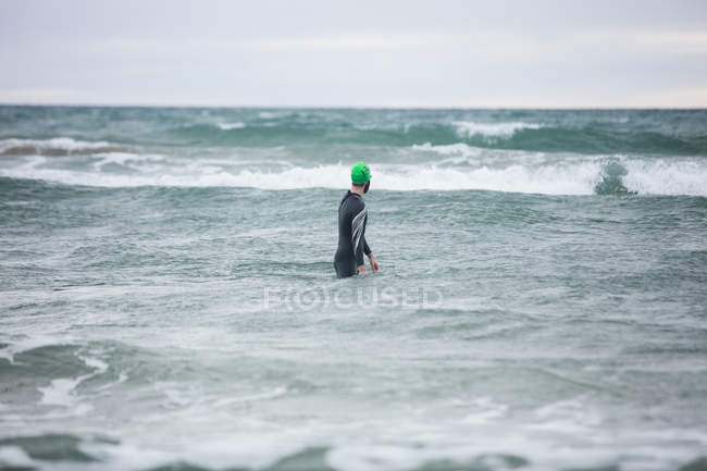 Вид сзади спортсмена в мокрых костюмах, стоящего в море — стоковое фото