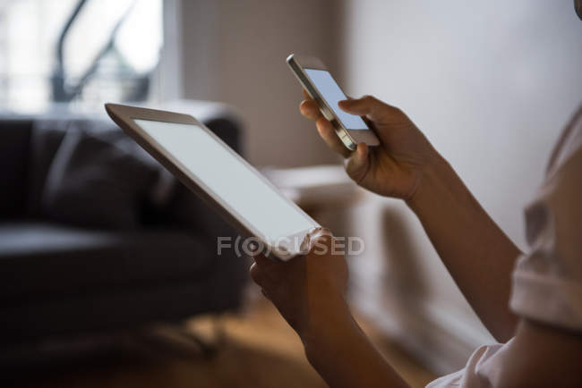 A meio da seção do homem usando tablet digital e telefone celular em casa — Fotografia de Stock