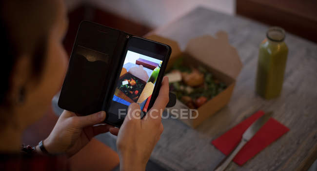 Woman clicking a photo of salad from mobile phone in cafe — Stock Photo