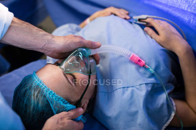 Руки лікаря розміщують кисневу маску на обличчі вагітної жінки в операційній кімнаті — стокове фото