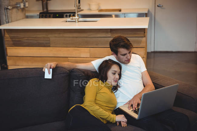 Casal alegre deitado juntos no sofá usando laptop na sala de estar — Fotografia de Stock