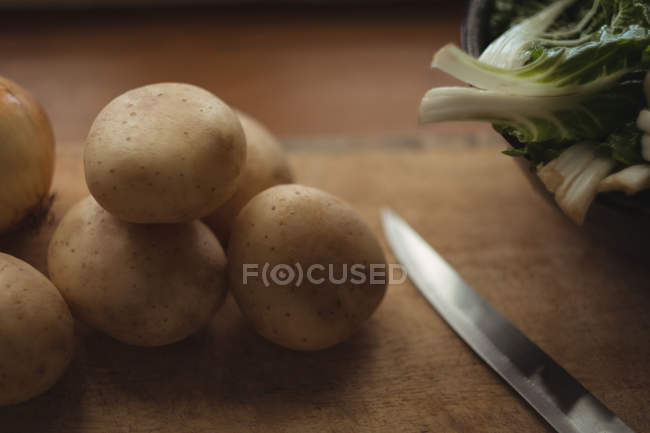 Крупный план картофеля, лука и салата на разделочной доске ножом — стоковое фото