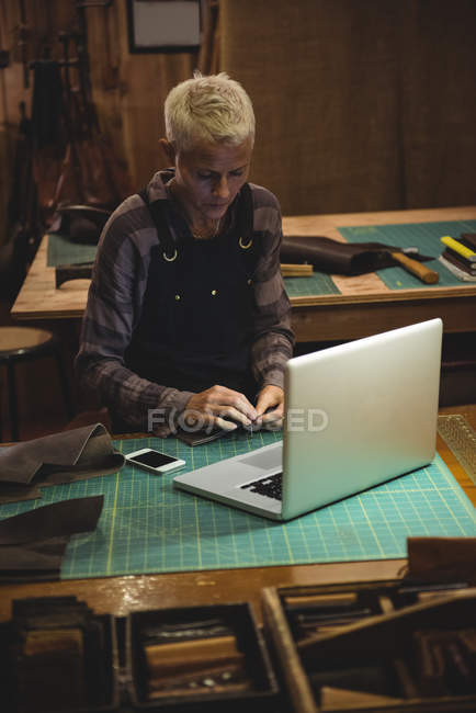 Mujer trabajando con portátil y teléfono móvil en la mesa en el taller - foto de stock