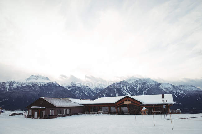 Maisons sur champ enneigé par les montagnes contre ciel nuageux — Photo de stock